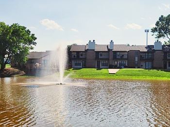 A fountain in the middle of a pond in front of a building.